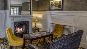 A room with a fireplace, yellow chairs, a table with magazines, and a framed picture on the wall. - The Ballymac Hotel (Lisburn)