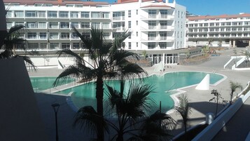 Un hotel con zona de piscina, palmeras y un edificio de varios pisos con balcones.
