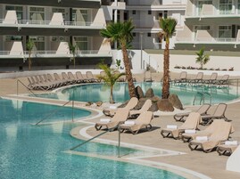 Zona de piscina con sillones reclinables y palmeras.
