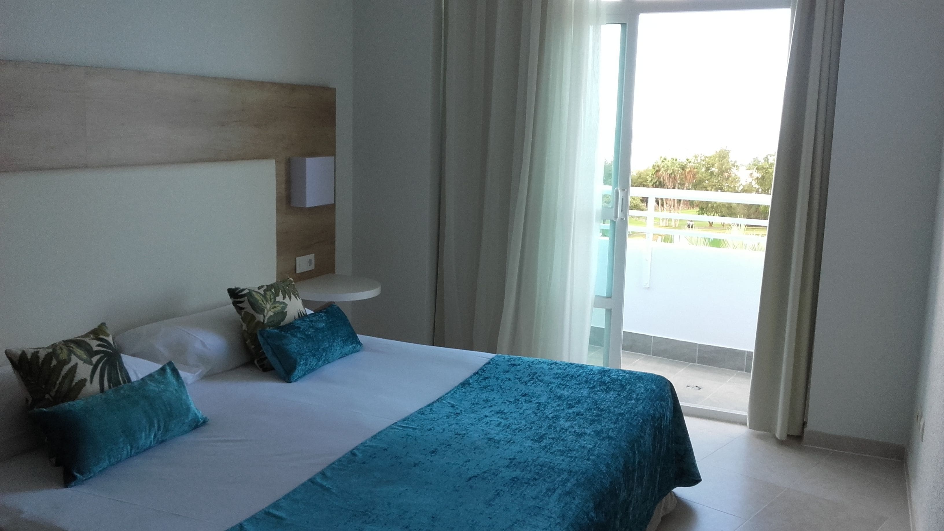 Ein Hotelzimmer mit einem Bett, Kissen, einem Nachttisch und Blick auf einen Balkon.