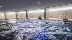 A large indoor hot tub with multiple jets, surrounded by a spacious area with a high ceiling and minimalistic design. - Gara Suites Golf & SPA (Arona)