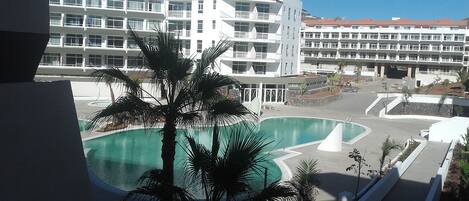 Un hotel con piscina, palmeras y un edificio de varios pisos con balcones.