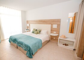 Habitación de hotel con una cama, una mesita de noche, un espejo y una pequeña estantería con un sombrero y zapatos.