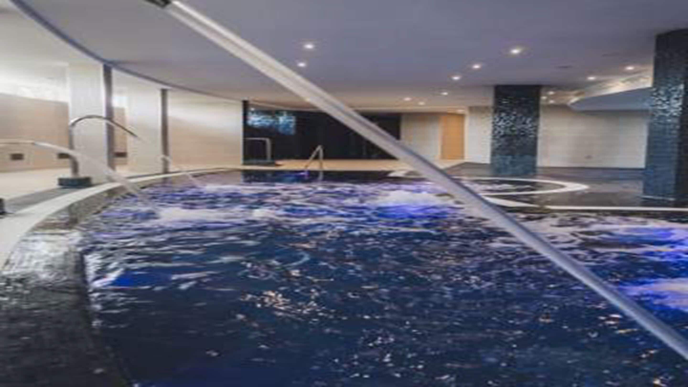 A modern indoor swimming pool with a central water feature and a sleek, contemporary design.