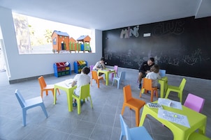 Un aula con sillas y mesas coloridas, una pizarra con escritura y vista a un patio de recreo.
