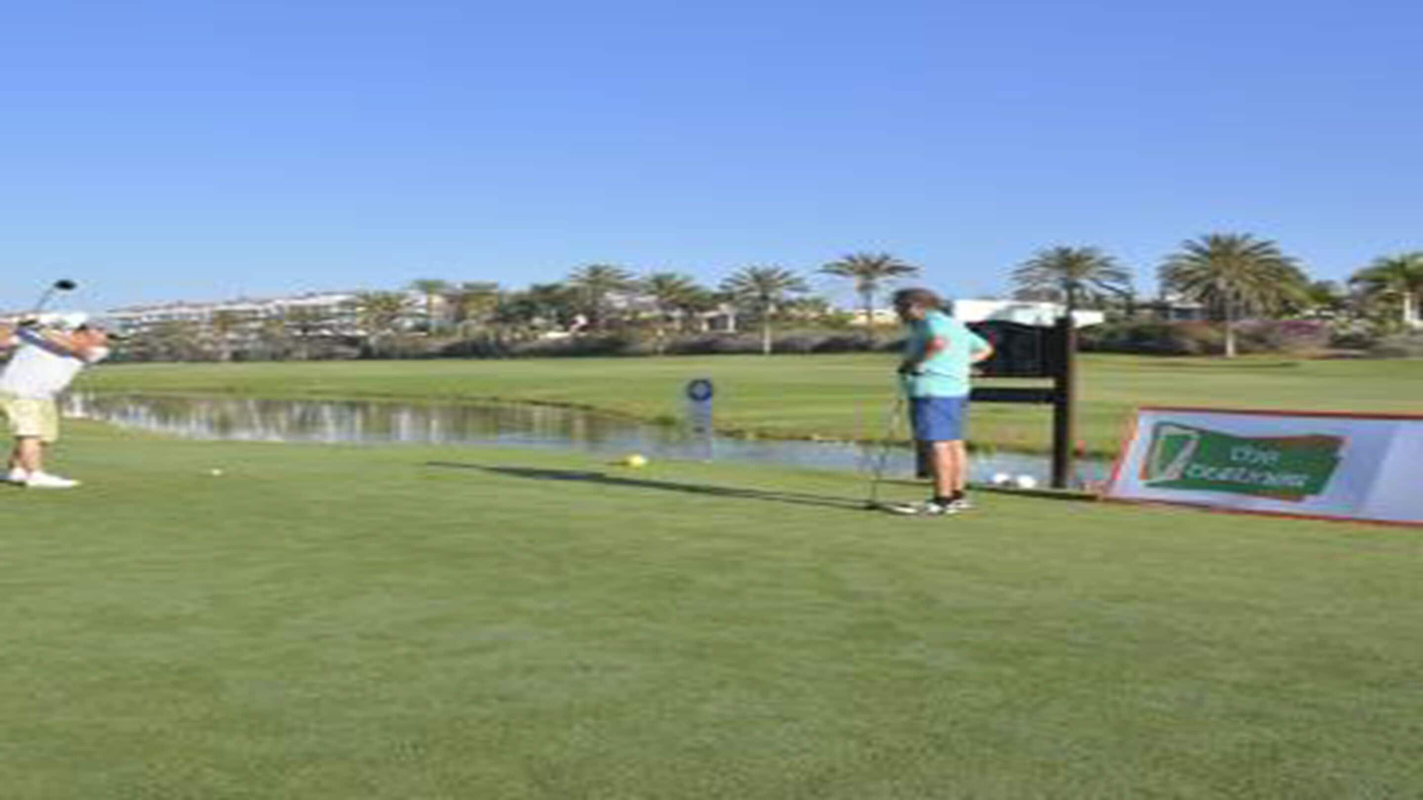 A golf course with a pond, a signboard, and palm trees in the background.