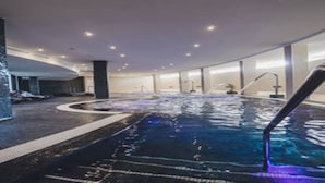 An indoor swimming pool with a curved design, clear water, and a tiled floor. - Gara Suites Golf & SPA (Arona)