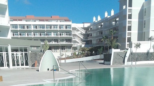 A clear blue pool with a modern design, surrounded by buildings with balconies and a clear sky. - Gara Suites Golf & SPA (Arona)