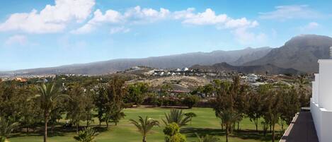 A golf course with palm trees, a mountain range, and a cityscape in the background.