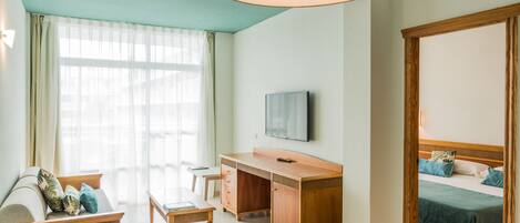 A hotel room with a wooden desk, a sofa, a bed, and a TV on the wall.