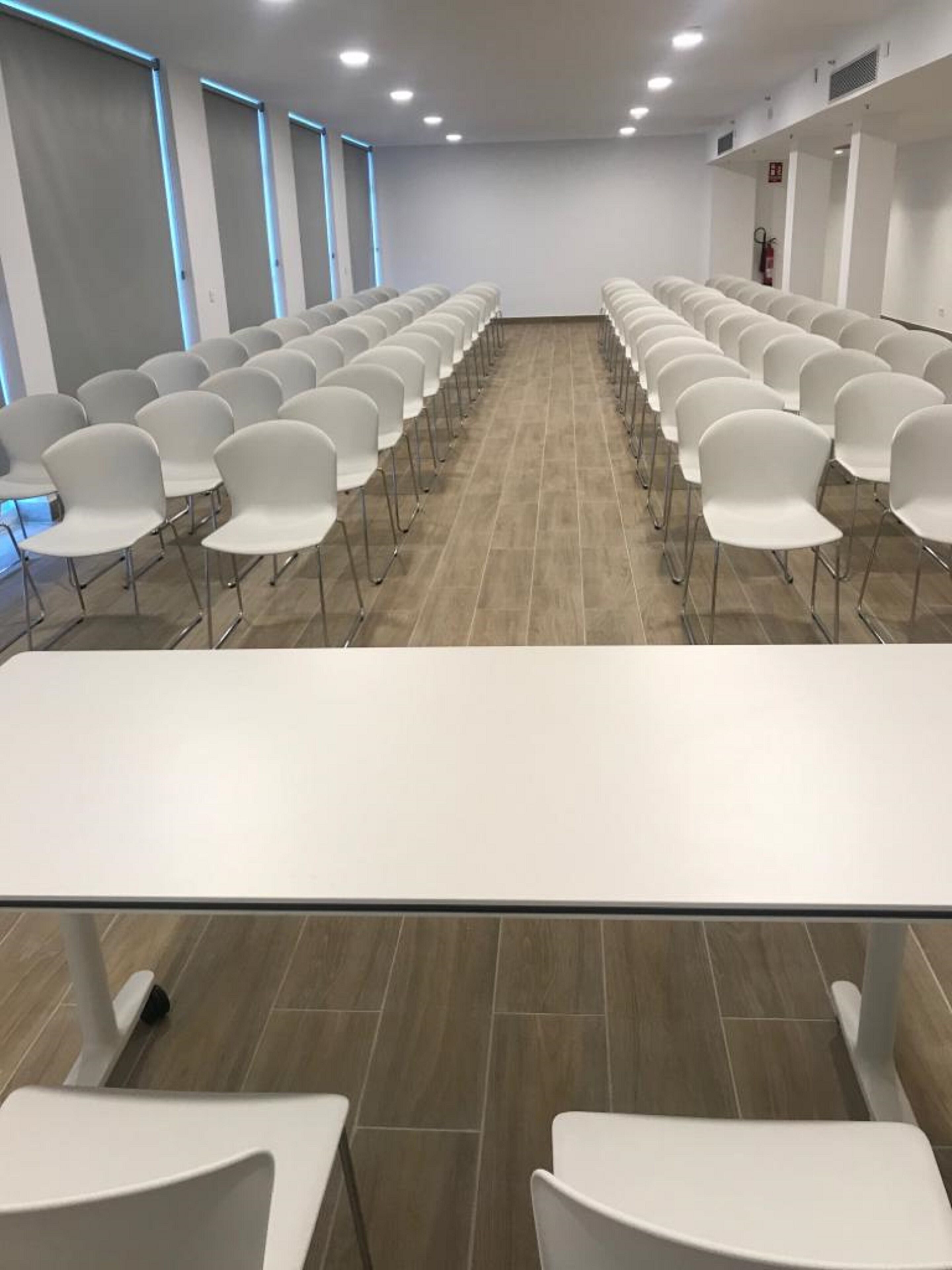 A conference room with rows of white chairs and a long table in the center.