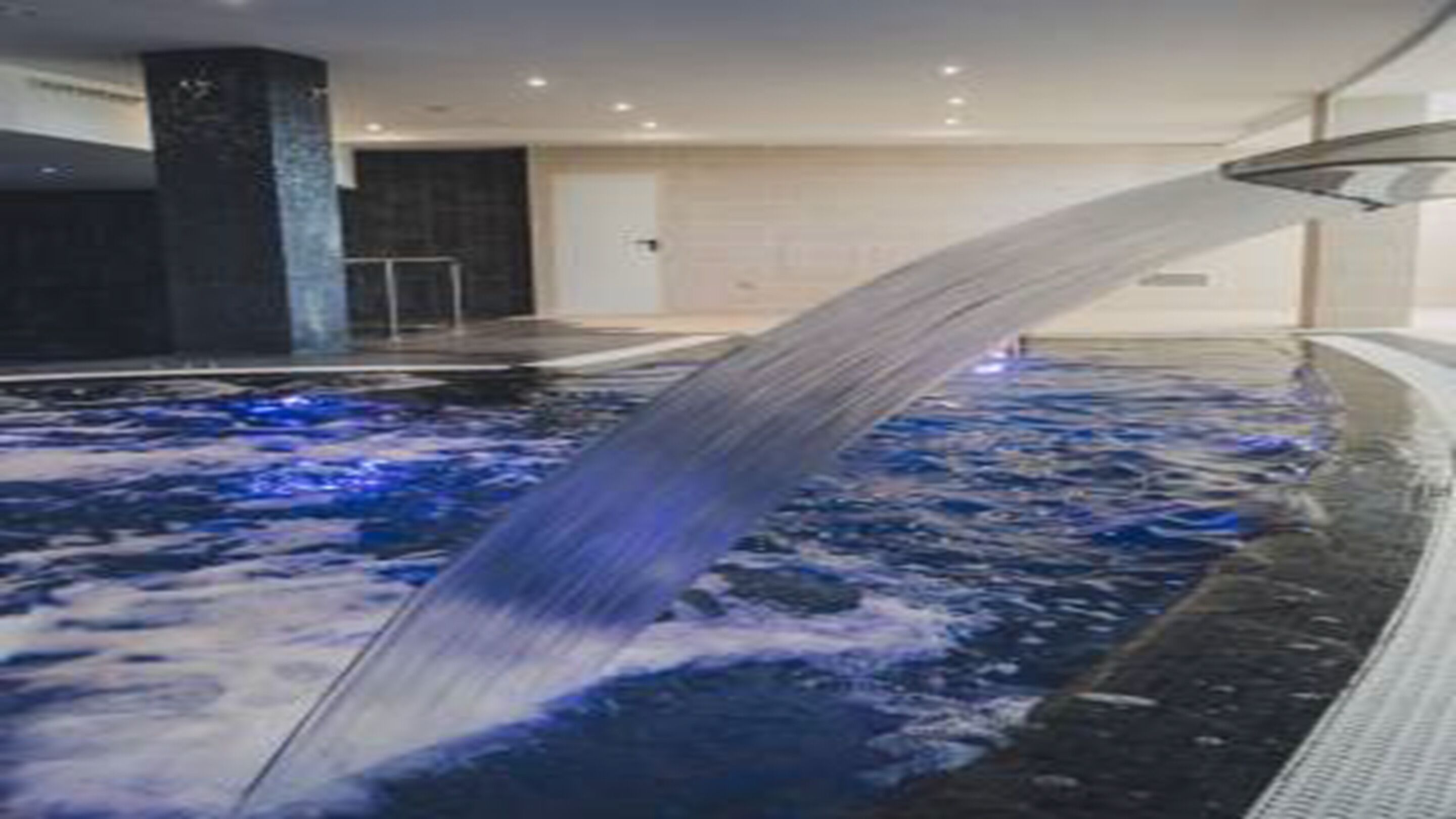 Una piscina interior moderna con un elemento acuático central y una vista despejada del borde.