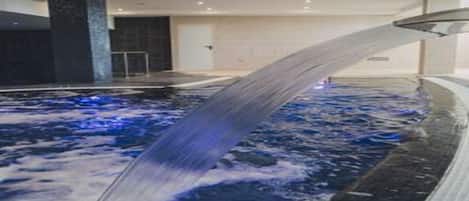 Una piscina interior moderna con un elemento acuático central y una vista despejada del borde.