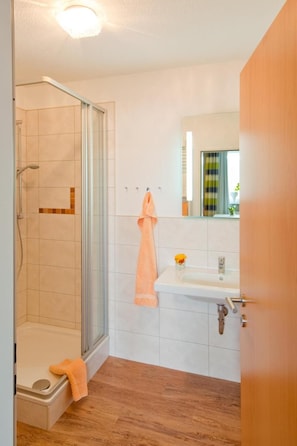 A bathroom with a glass shower enclosure, a sink with a mirror, and a wooden floor. - Waldhotel Wiesemann (Waldeck)