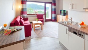 A modern kitchen with a wooden countertop, a sink, and a dishwasher. There is a dining area with a table and chairs, and a red sofa. The room has large windows with curtains, offering a view of the outdoors. - Waldhotel Wiesemann (Waldeck)