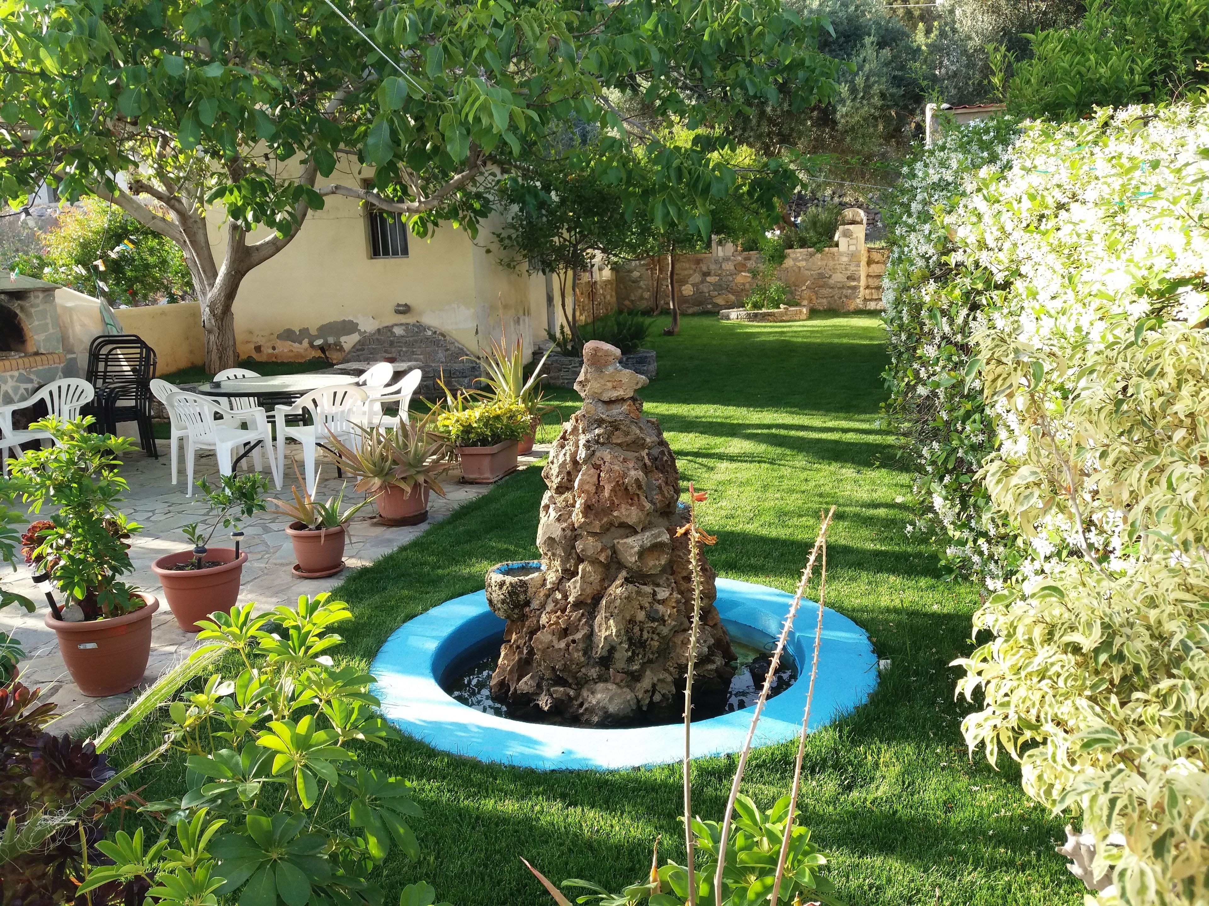 A garden with a central rock feature, potted plants, and a stone wall.