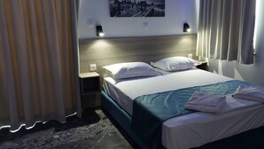 Una habitación de hotel con cama, mesita de noche y una lámpara fijada a la pared.