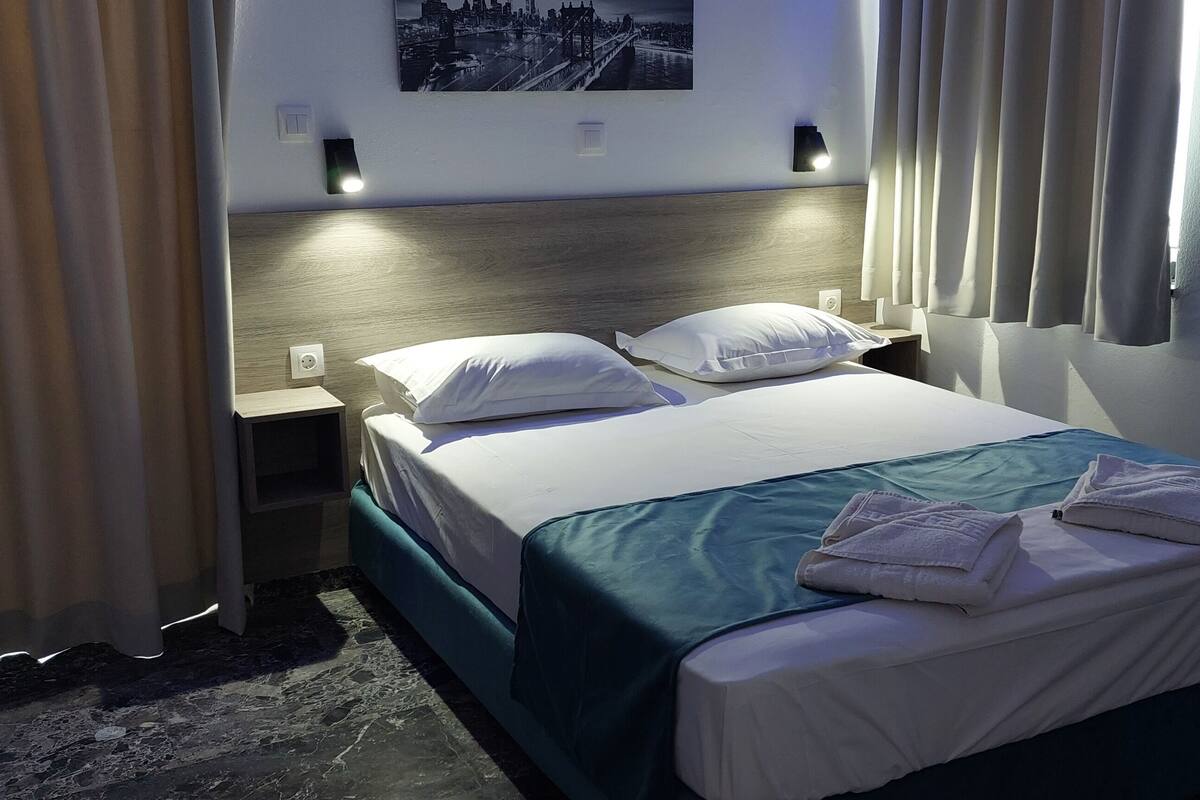 A hotel room with a bed, nightstand, and a wall-mounted light.