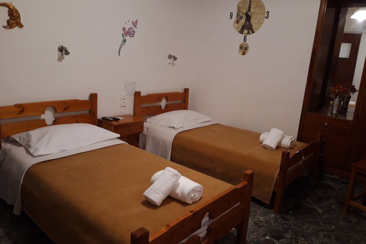 A hotel room with two wooden beds, white linens, a wall clock, and a small decorative item.