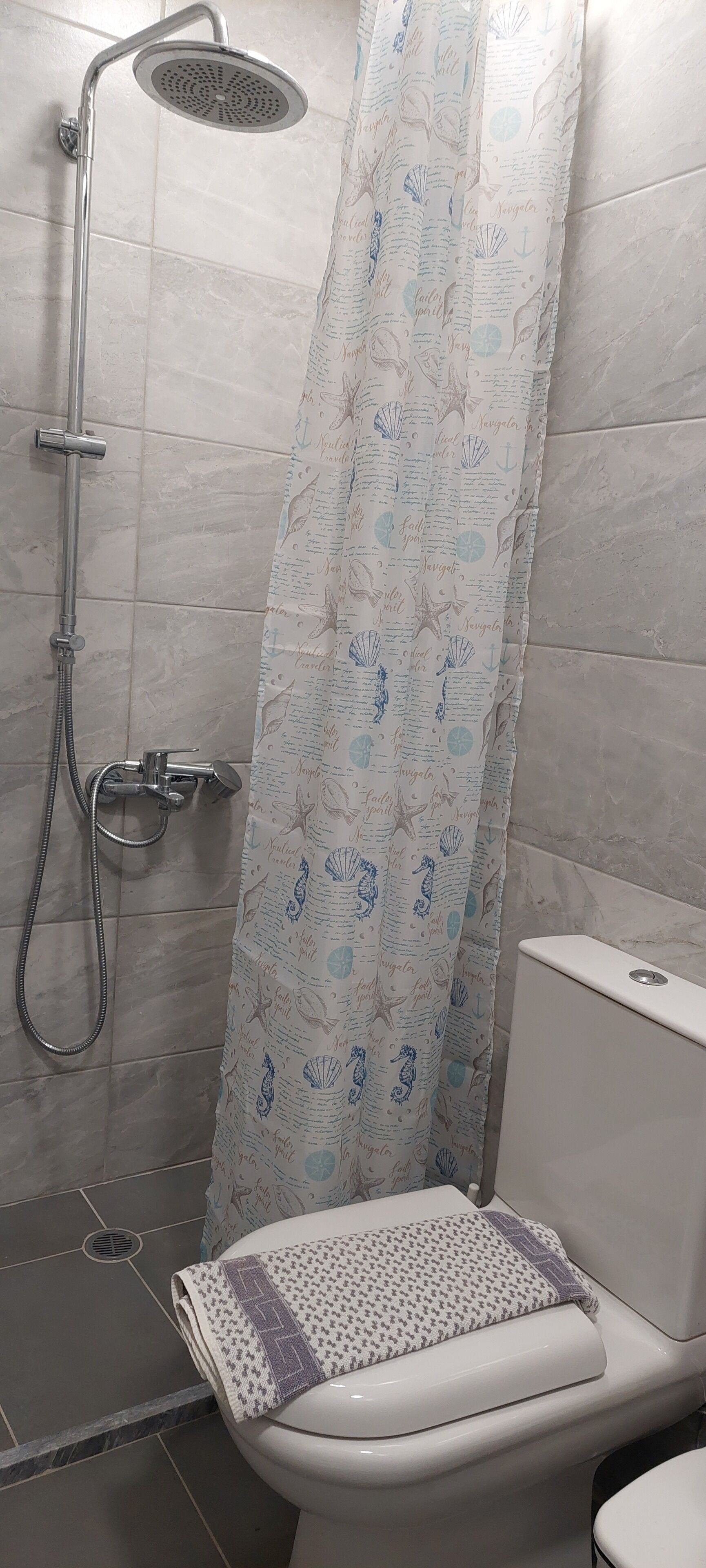 Un bagno con doccia, servizi igienici e una tenda decorata con motivi marittimi.