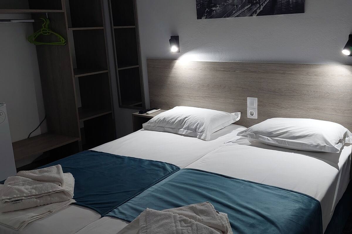 A hotel room with a bed, two bedside tables, a nightstand, a wardrobe, and a wall-mounted shelf.