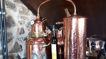 A copper distillation apparatus and a bottle of wine on a wooden table against a stone wall.