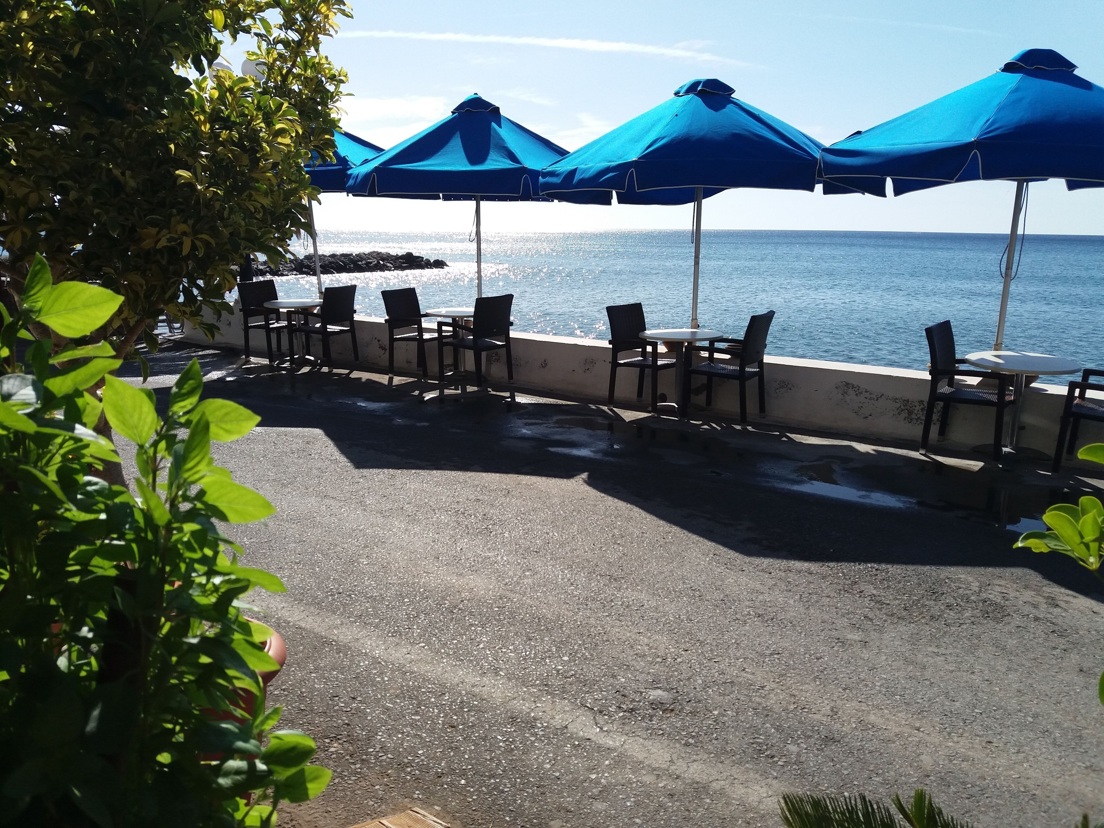 Un patio frente al mar con asientos exteriores y sombrillas.