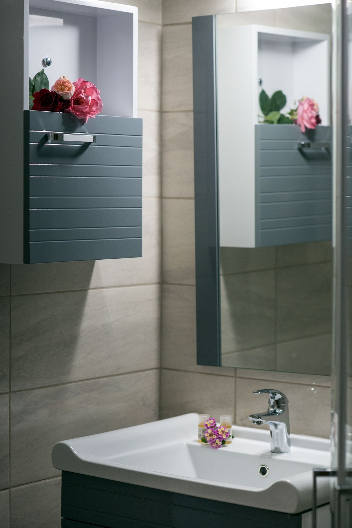 A bathroom with a white sink, a mirror, and a cabinet with flowers.