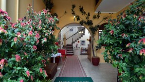 Un hall d’hôtel avec un tapis où est écrit « BIENVENUE », un escalier et des plantes en pot.