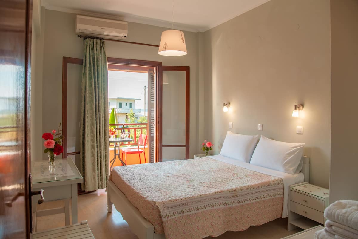A bedroom with a bed, bedside tables, a nightstand, a window with curtains, and a view of the outside.