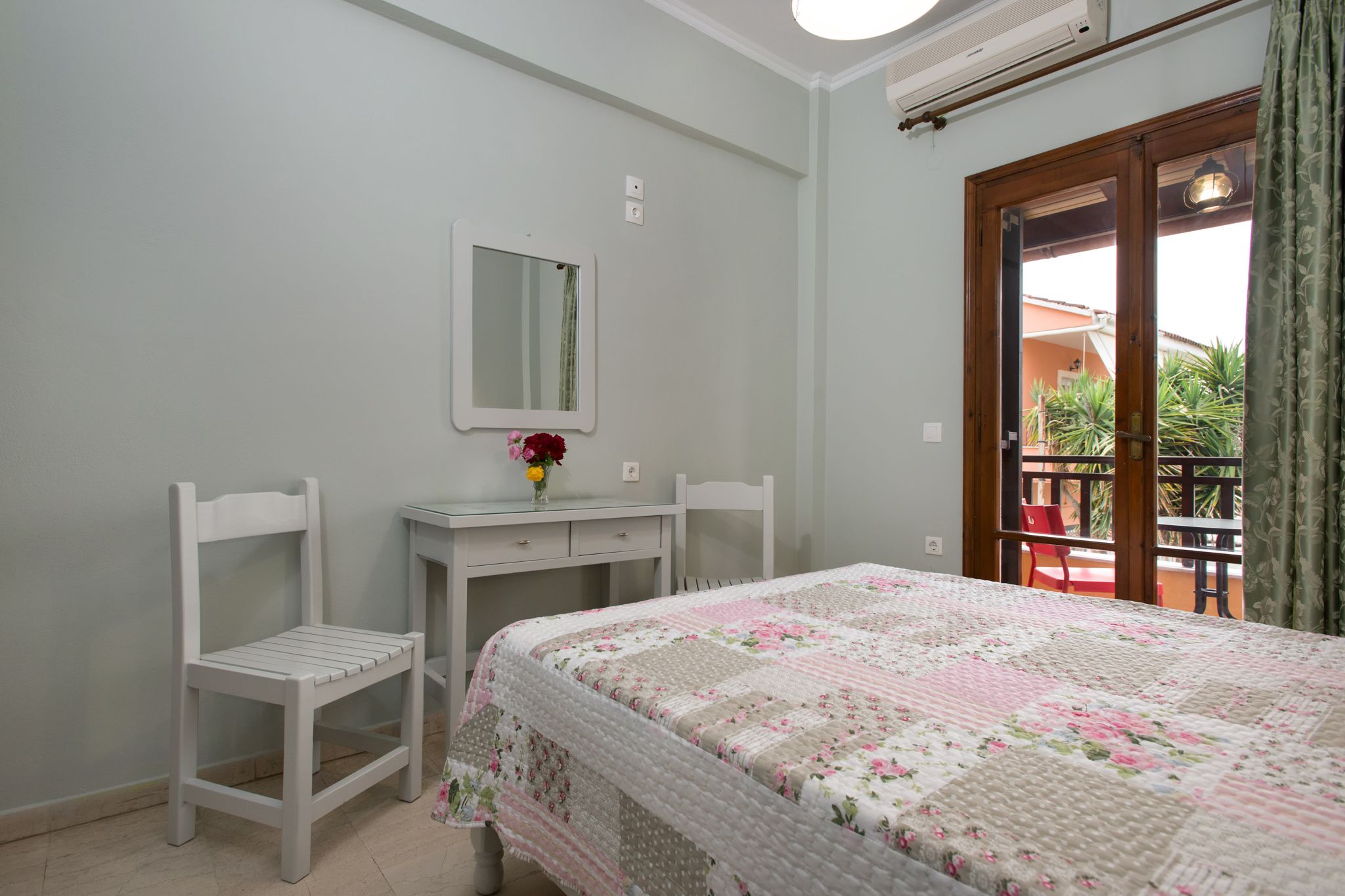 A bedroom with a bed, two chairs, a dresser, a mirror, and a window with a view of the outside.