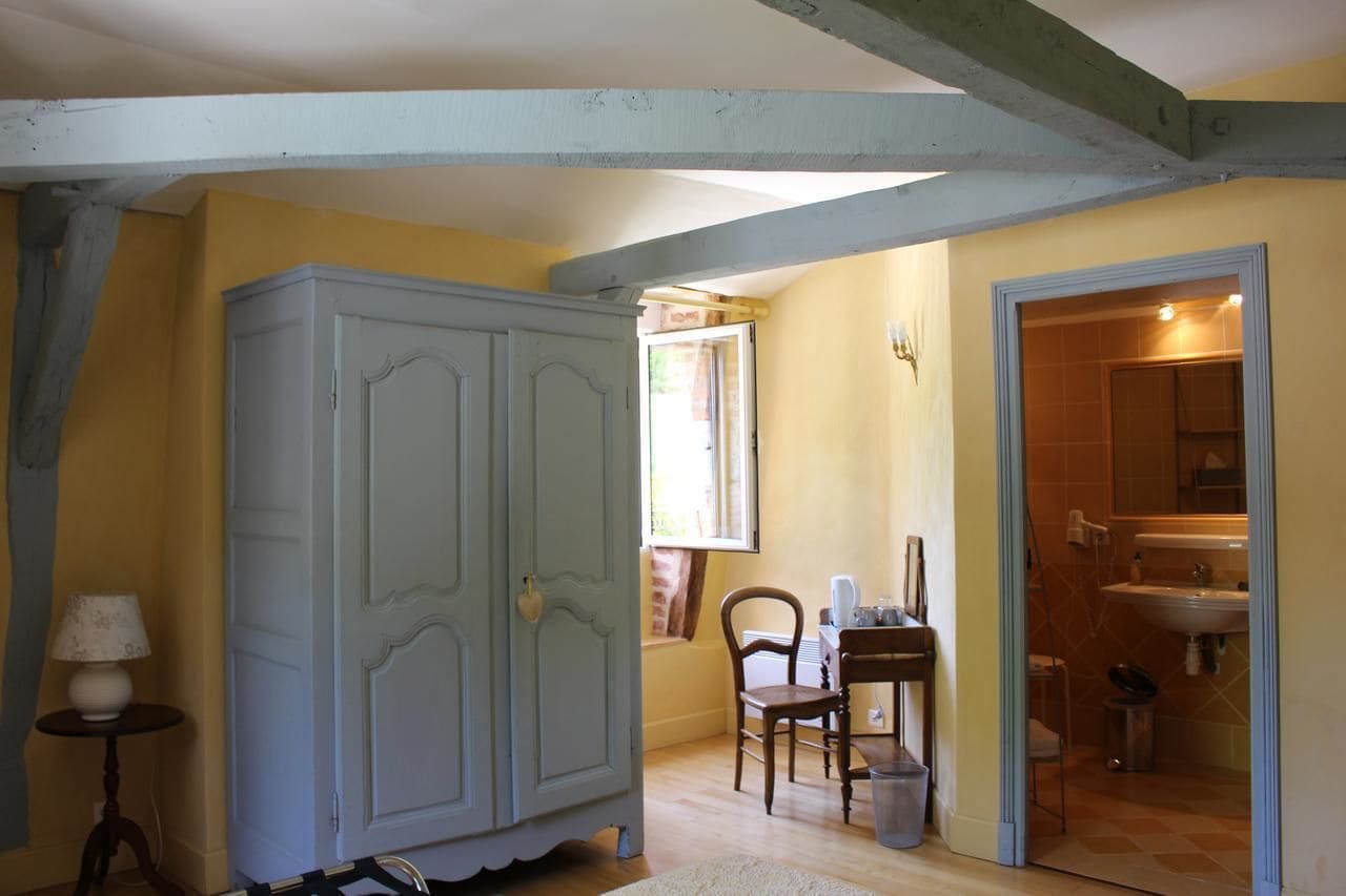 Una habitación con un armario grande, una mesita con una lámpara, una ventana y un baño visible a través de una puerta abierta.