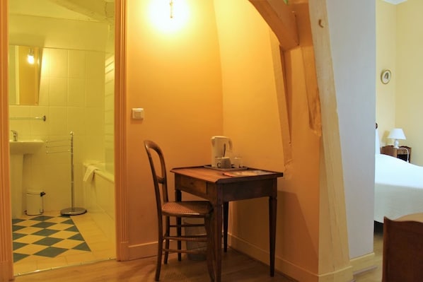A hotel room with a wooden table, a chair, a bed, and a bathroom visible through an open door. - Maison d'hôtes Redon (Tour-de-Faure)