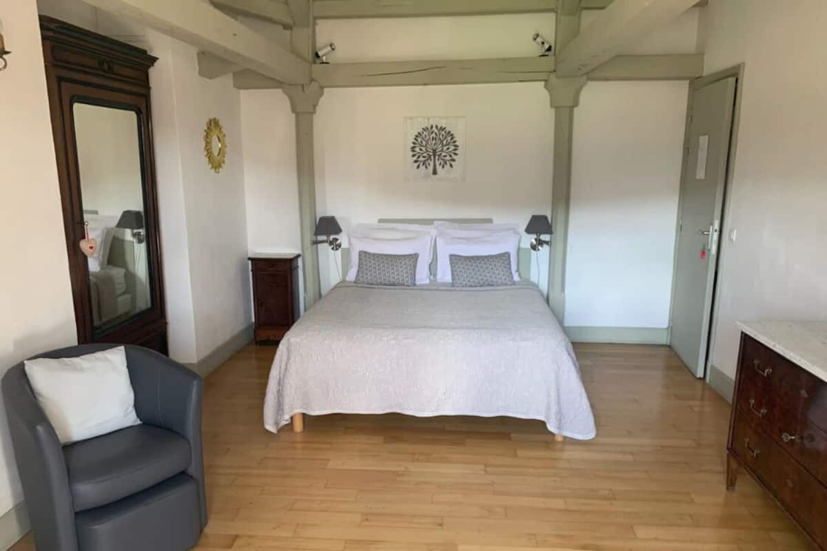 A bedroom with a large bed, a chair, a dresser, and a mirror.