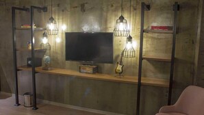 A room with a wooden shelf holding a television, a globe, and a guitar. There are two metal stands with hanging lights. - Meydan Besiktas Hotel (Istanbul)