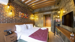 A hotel room with a brick wall, wooden ceiling beams, a bed with white linens, a purple throw blanket, a bedside phone, and a TV on a wooden shelf. - Meydan Besiktas Hotel (Istanbul)