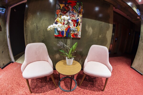 A room with two white chairs, a small wooden table with a potted plant, and a colorful abstract painting on the wall. - Meydan Besiktas Hotel (Istanbul)