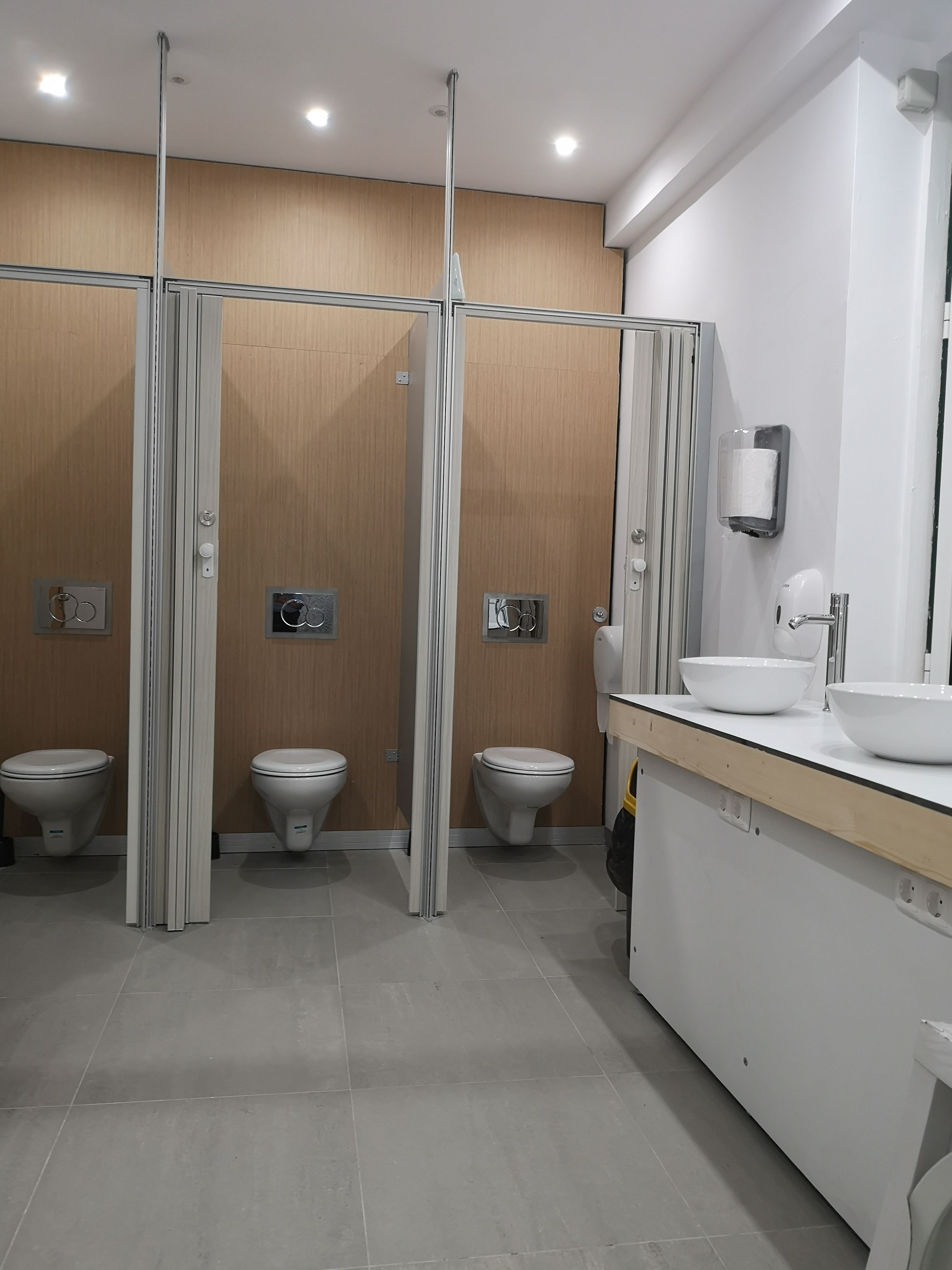 A modern bathroom with three toilets, a sink, and a mirror.
