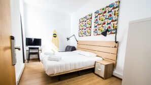 A neatly arranged bedroom with a bed, bedside table, lamp, and a surfboard against the wall. - Stay With Me Hostel (Lisbon)