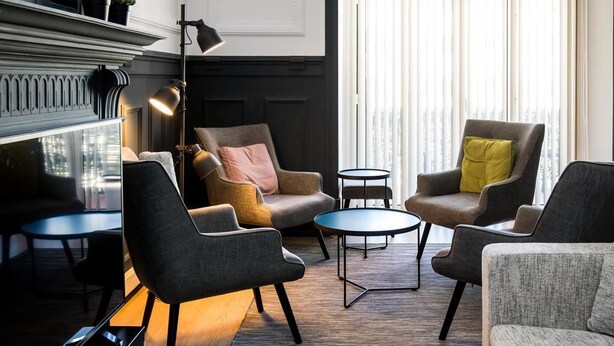 A modern lounge area with a fireplace, two armchairs, a small round table, and a floor lamp. - Stay With Me Hostel (Lisbon)