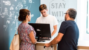 A reception desk with a "STAY WITH ME" sign, a laptop, and a person standing. - Stay With Me Hostel (Lisbon)