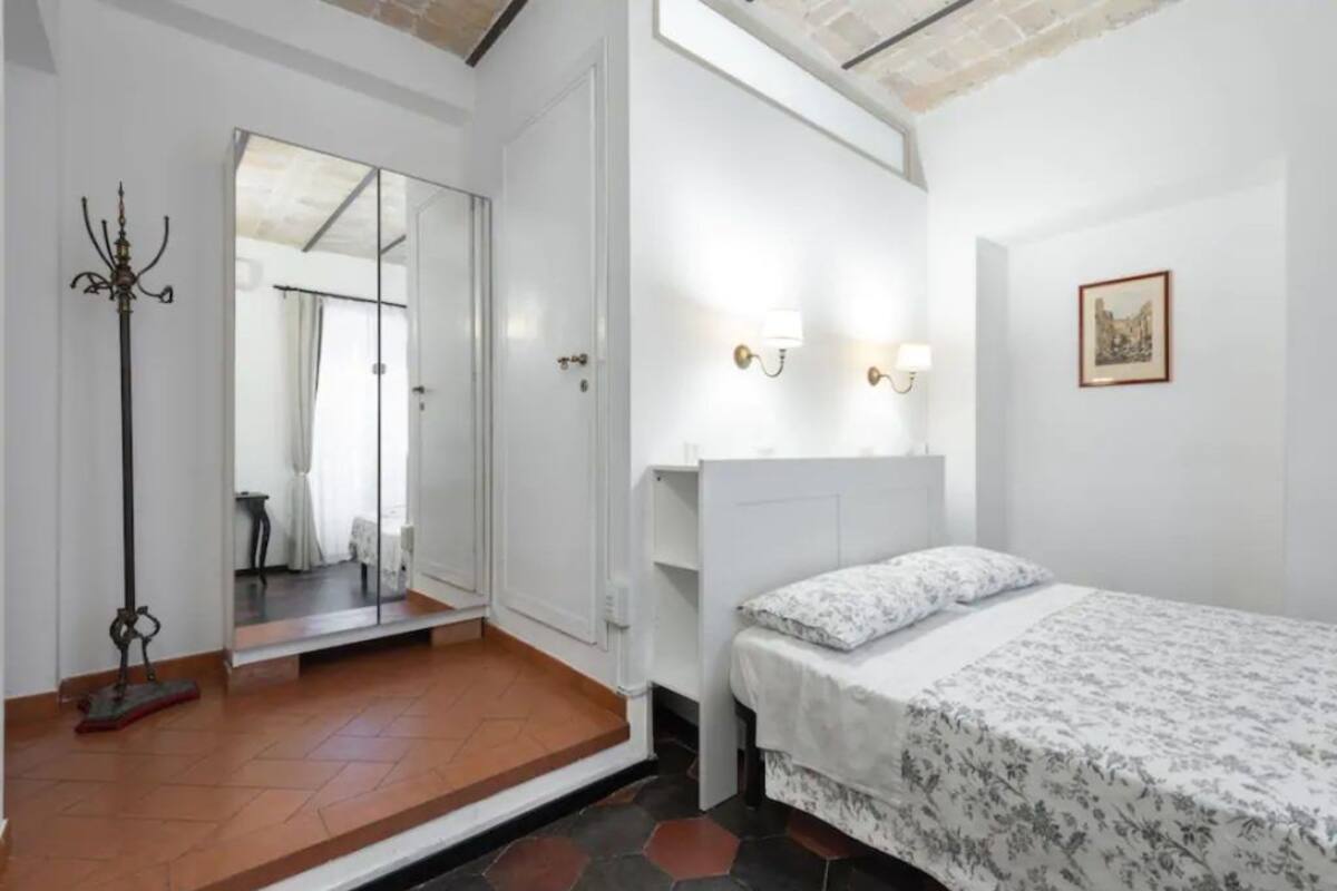 Un dormitorio con cama, espejo, perchero y puerta que da a otra habitación.