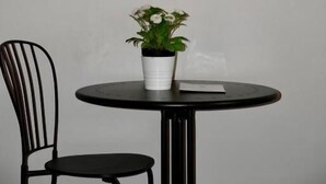 Een ingelijste historische illustratie aan een muur, een ronde zwarte tafel met een plant in pot, en een zwarte stoel.