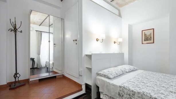 Een slaapkamer met een bed, een spiegel, een nachtkastje en een wandlamp.