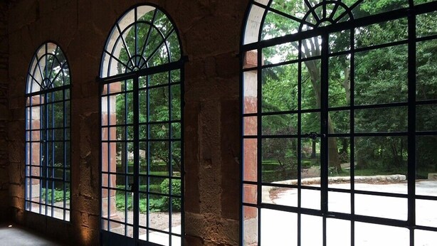 A room with large arched windows with metal grilles, stone walls, and a view of a garden. - Domaine de Saint Charles (Les Plans)