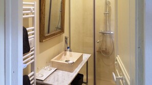 Un baño con lavamanos de mármol, un espejo, toallero y ducha.