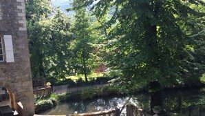A stone building with a courtyard featuring a water body, surrounded by lush greenery and a stone fence. - Domaine de Saint Charles (Les Plans)
