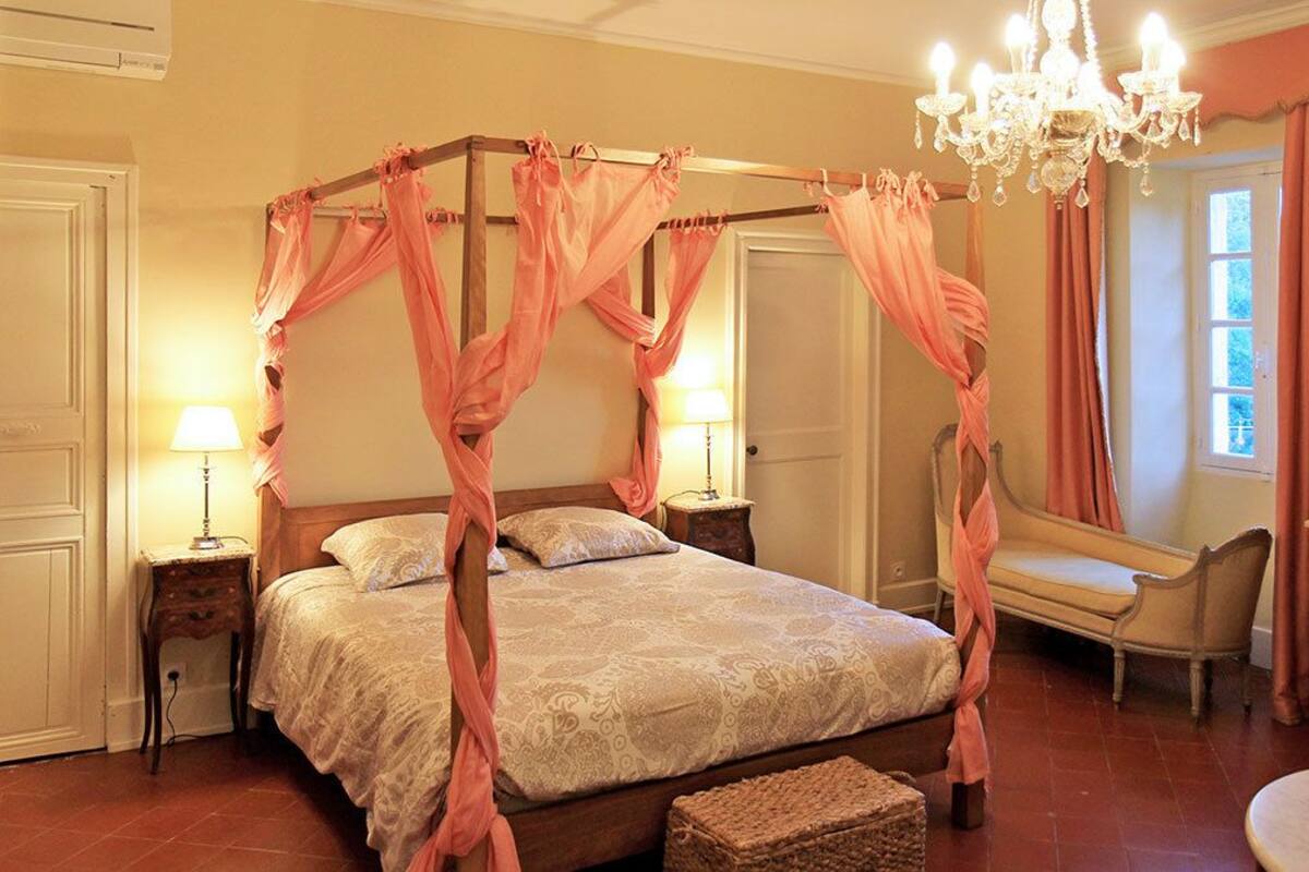 A four-poster bed with a canopy, bedside tables, a chair, a dresser, and a chandelier.