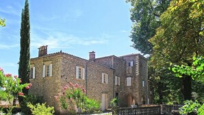 A stone building with a garden, featuring a tall cypress tree and flowering plants. - Domaine de Saint Charles (Les Plans)