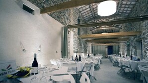 A spacious banquet hall with high ceilings and stone walls, featuring round tables set for dining. - Domaine de Saint Charles (Les Plans)